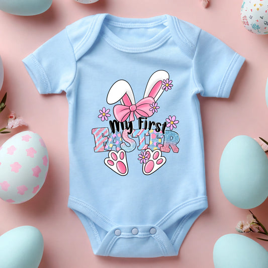 Light blue baby onesie with Easter design on a pink background with Easter eggs and flowers.