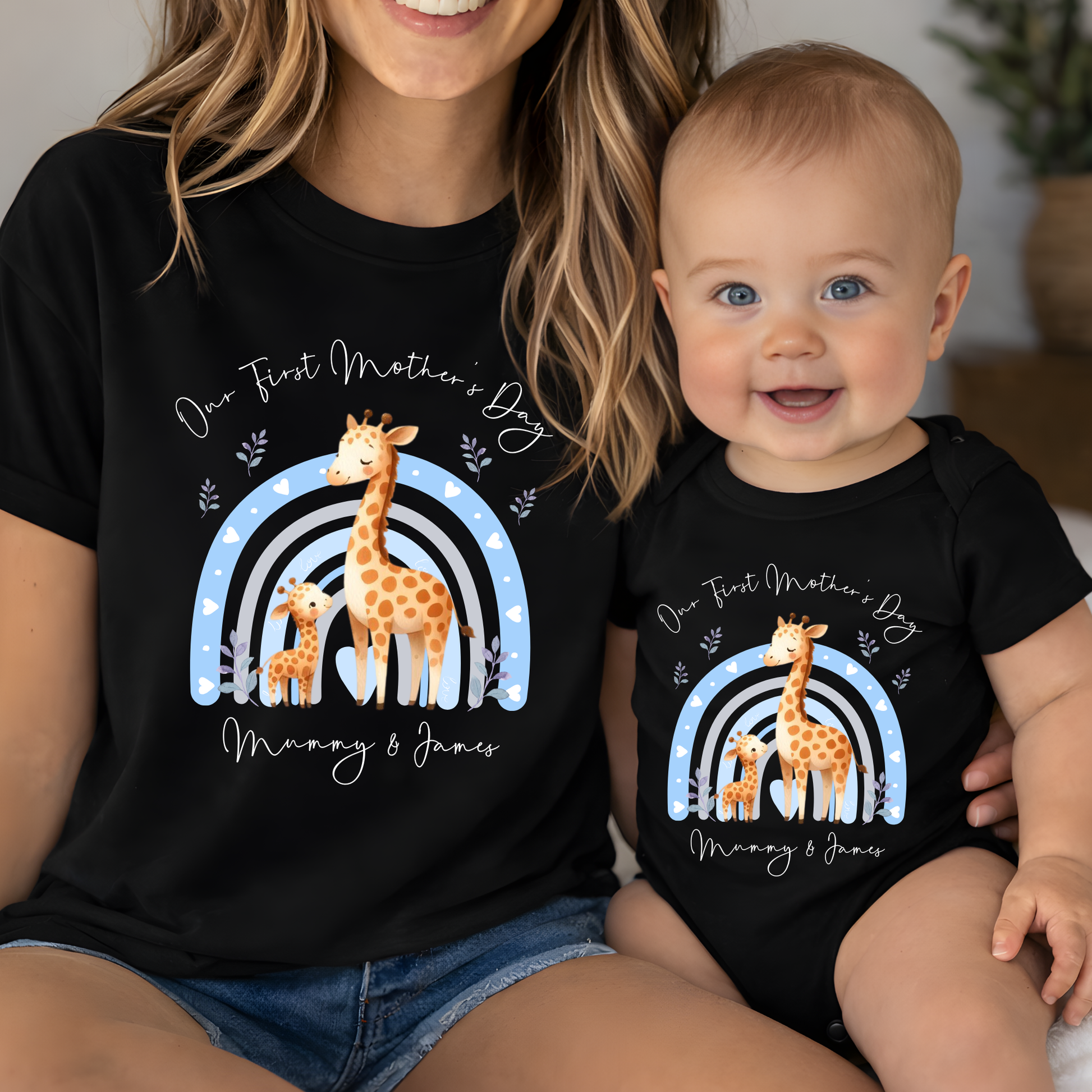 Woman and baby wearing matching black t-shirts with giraffe design and 'First Mother's Day' text.
