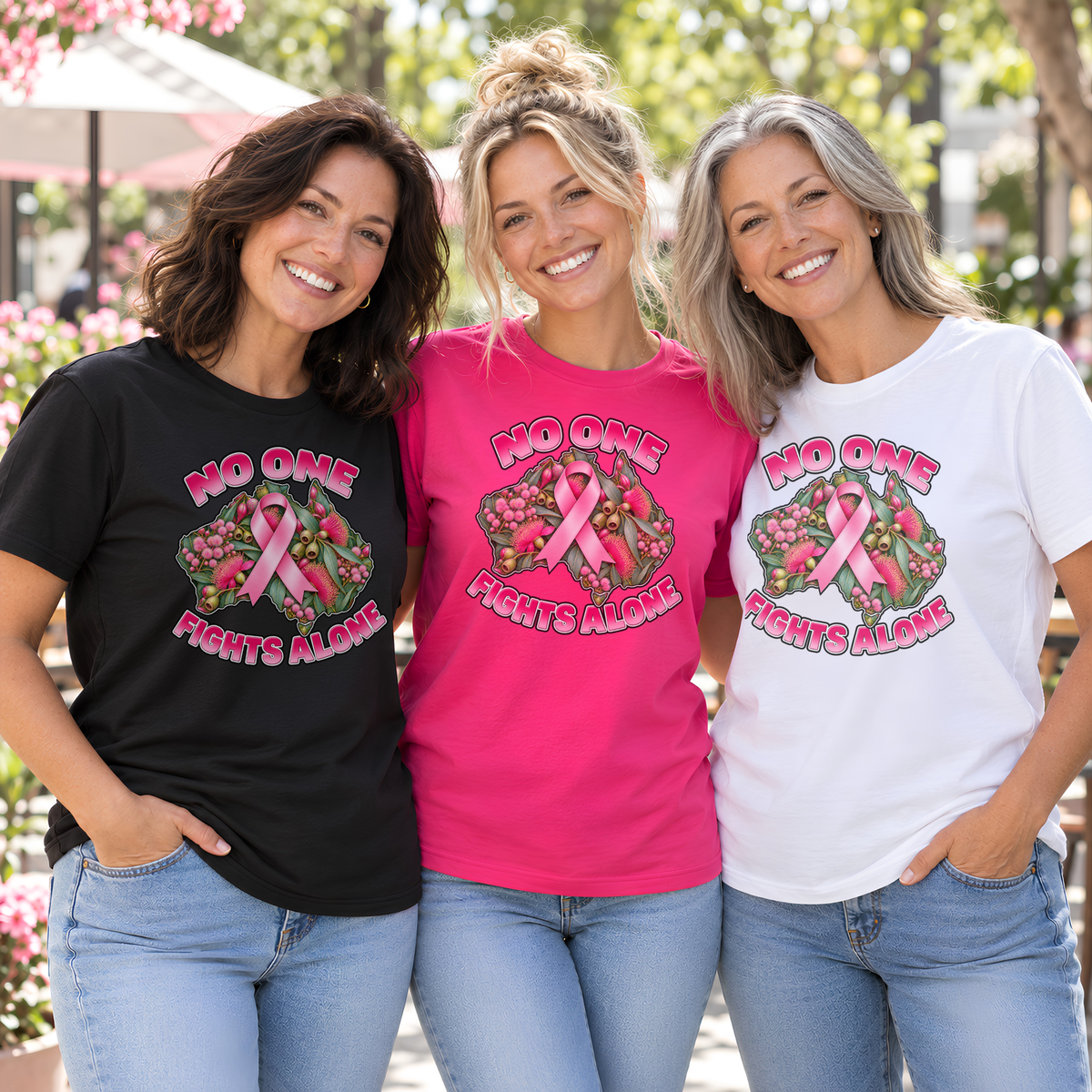 Three women wearing No One Fights Alone breast cancer awareness shirts in black, fuchsia and white